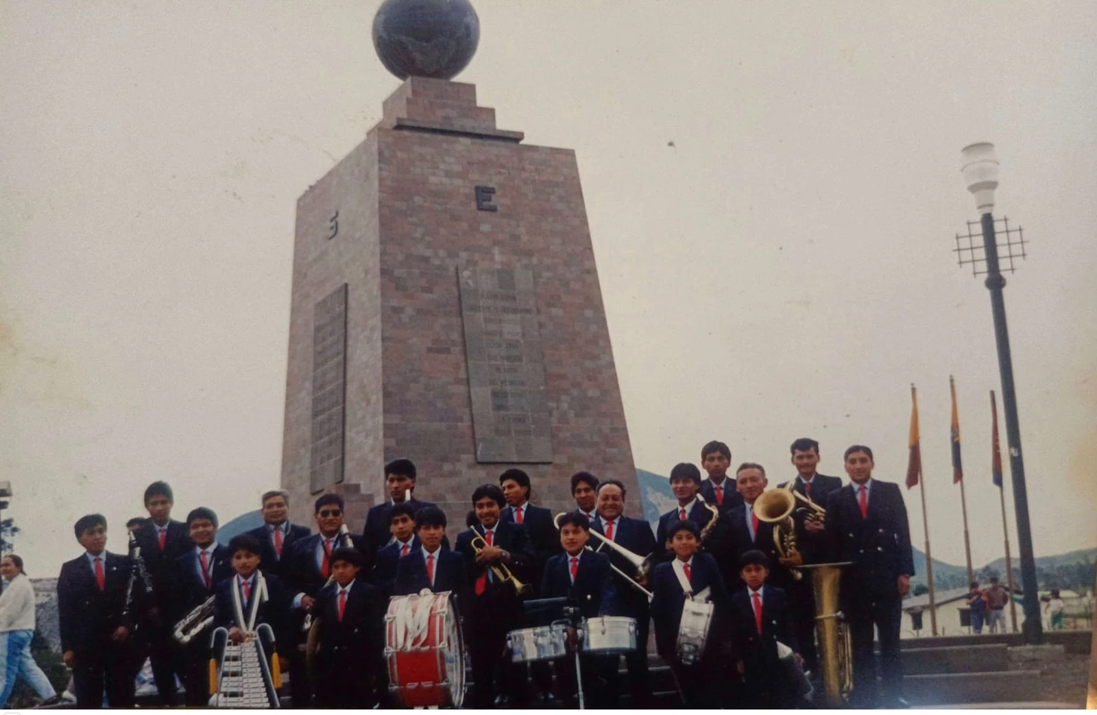 Formación histórica de la banda con instrumentos frente al monumento de la Mitad del Mundo.