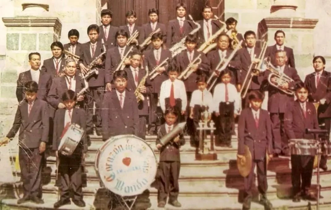 Formación histórica de la banda con varias generaciones de músicos frente a una iglesia.