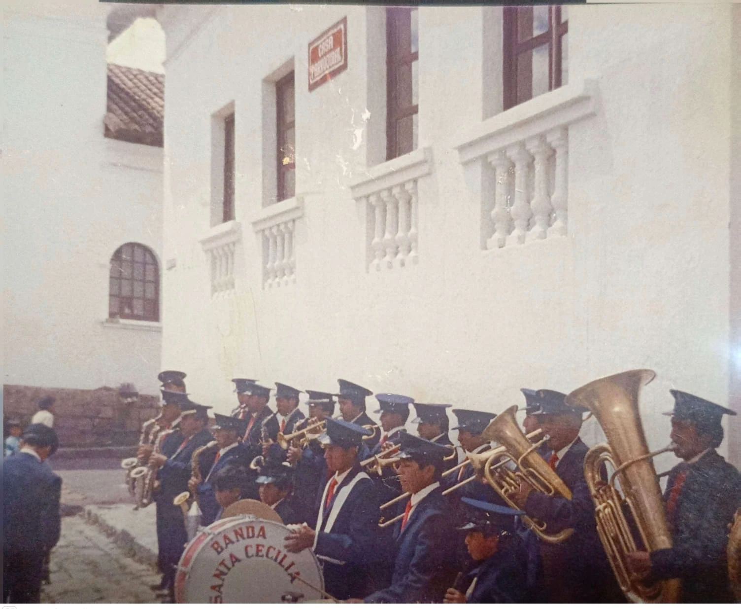 Formación antigua de la Banda Santa Cecilia con instrumentos frente a un edificio.